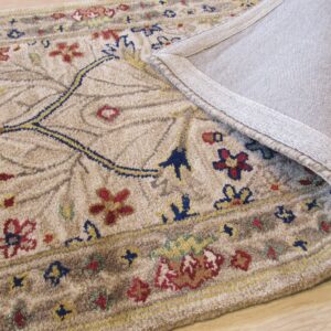 Textured tan rug with a traditional floral design, folded over to expose the gray woven backing on wood flooring.
