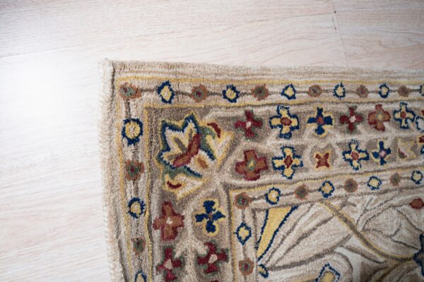 Textured beige rug detail featuring stylized floral and geometric patterns in blue, yellow, and red on light wood.