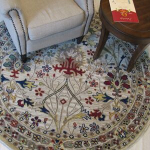 Round beige and multicolored floral rug beneath a nailhead trim armchair and dark wood side table.
