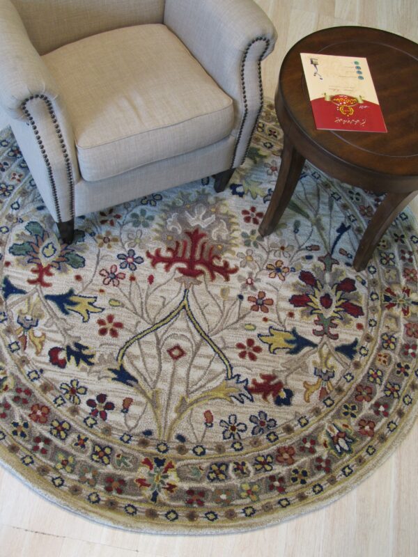 Round beige and multicolored floral rug beneath a nailhead trim armchair and dark wood side table.