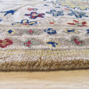 Close view of a thick, beige rug border with blue, red, and yellow floral patterns resting on wood flooring.