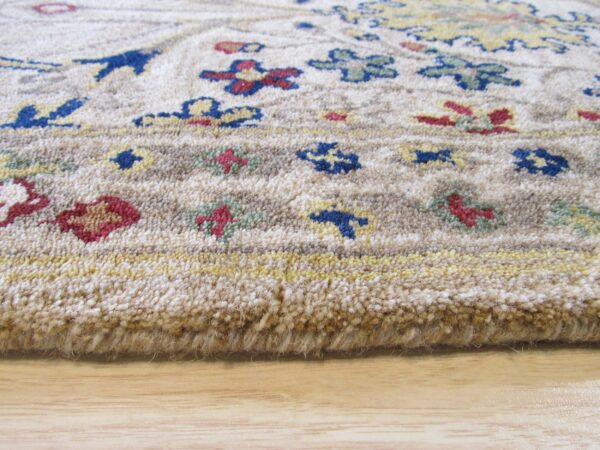 Close view of a thick, beige rug border with blue, red, and yellow floral patterns resting on wood flooring.