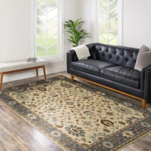 A cream floral rug with a gray border rests on wood flooring beside a black tufted leather sofa.