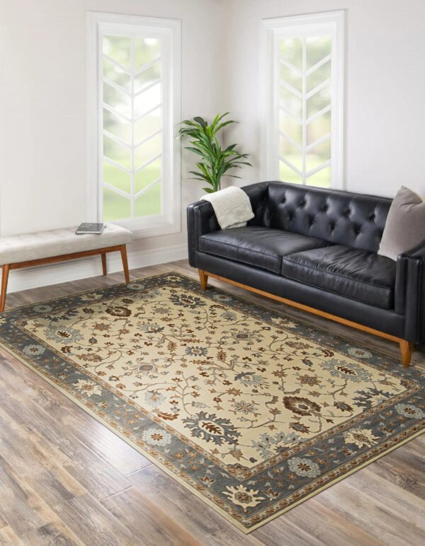 A cream floral rug with a gray border rests on wood flooring beside a black tufted leather sofa.