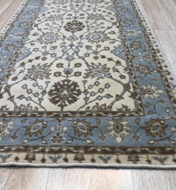 Cream runner rug featuring a traditional floral pattern and blue border on light wood planks.