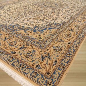 Angled view of a detailed beige and blue traditional rug featuring scrolling floral patterns on light wood flooring.