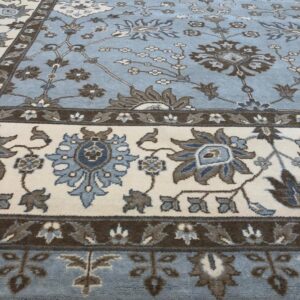 Light blue traditional rug featuring floral designs in cream, brown, and slate blue tones on wood flooring.