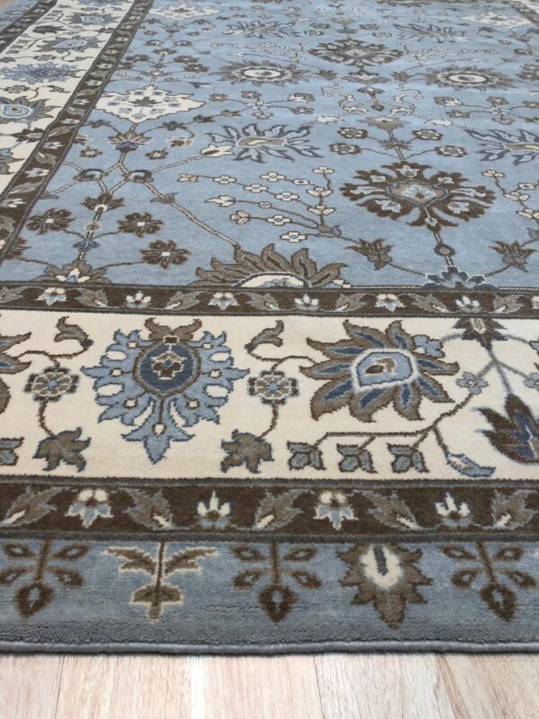 Light blue traditional rug featuring floral designs in cream, brown, and slate blue tones on wood flooring.