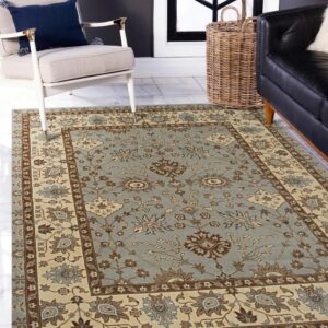 Dusty blue and cream traditional floral rug on white tile, framed by a beige armchair.