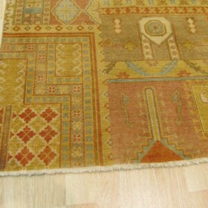 Low-pile rug with geometric patterns in gold, rust, and muted blue lies on blonde wood.