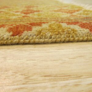 Yellow and orange patterned rug edge with medium pile rests on blonde wood flooring.