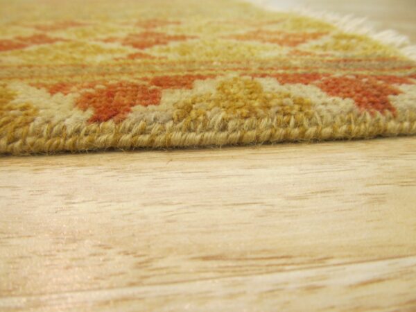 Yellow and orange patterned rug edge with medium pile rests on blonde wood flooring.