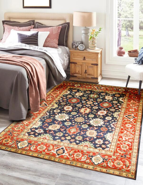 A traditional navy and red floral rug lies on gray wood floor in a brightly lit bedroom.