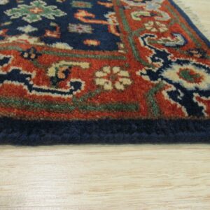 Ornate navy and rust traditional rug border detail rests on light blonde wooden flooring.