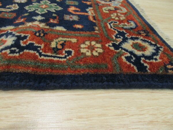Ornate navy and rust traditional rug border detail rests on light blonde wooden flooring.