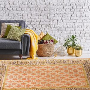 Terracotta and cream geometric rug grounding a living area with a gray sofa and white brick wall.