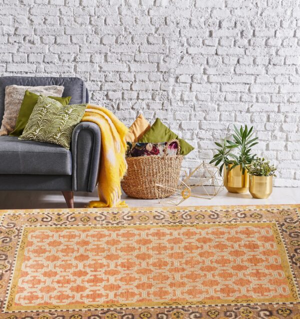 Terracotta and cream geometric rug grounding a living area with a gray sofa and white brick wall.