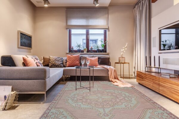 Muted pink rug featuring a large teal traditional medallion pattern anchors a modern gray sectional sofa.