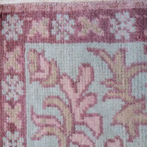 High-pile rug corner featuring dusty rose, pale blue, and tan floral designs on light wood flooring.