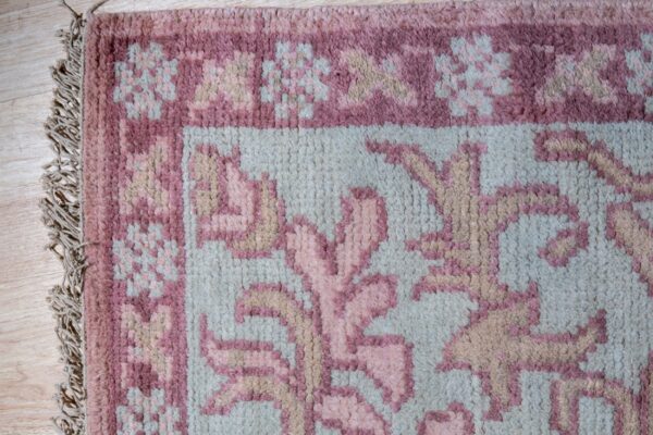 High-pile rug corner featuring dusty rose, pale blue, and tan floral designs on light wood flooring.