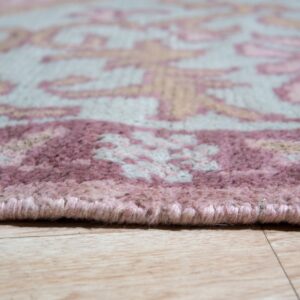 Close-up of a light gray rug with pink and beige floral patterns and a bound edge on wood flooring.
