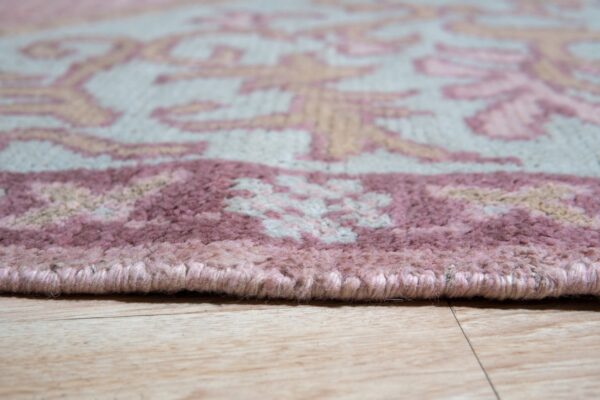 Close-up of a light gray rug with pink and beige floral patterns and a bound edge on wood flooring.