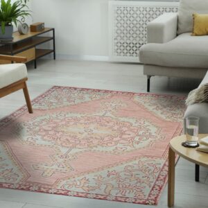 A distressed pink and cream traditional rug is layered on light wood flooring in a cozy living room.