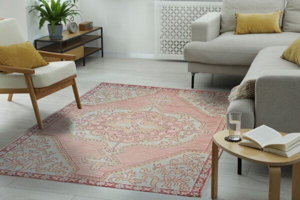 A distressed pink and cream traditional rug is layered on light wood flooring in a cozy living room.
