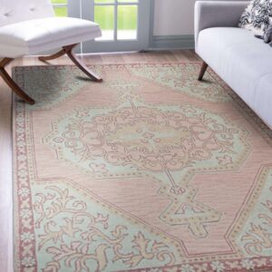 A pink and mint medallion rug on wood floors next to a white chair and a gray sofa.