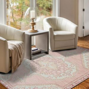 A pink and light blue patterned rug sits between two white chairs on hardwood floors near a window.