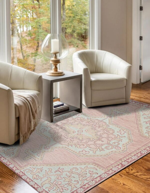 A pink and light blue patterned rug sits between two white chairs on hardwood floors near a window.