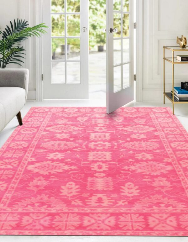 A vibrant pink and light patterned rug spans the white floor in a bright entryway with french doors.