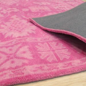 Bright pink rug featuring a distressed floral pattern and gray backing shown on light wood floors.