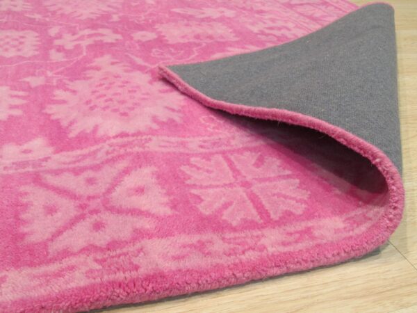 Bright pink rug featuring a distressed floral pattern and gray backing shown on light wood floors.