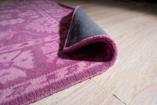 High pile pink and magenta patterned rug corner lifted, revealing gray backing on light wood floor.