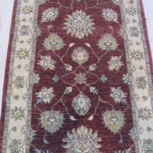 Deep burgundy runner rug featuring intricate cream, sage, and blue floral patterns on pale wood flooring.