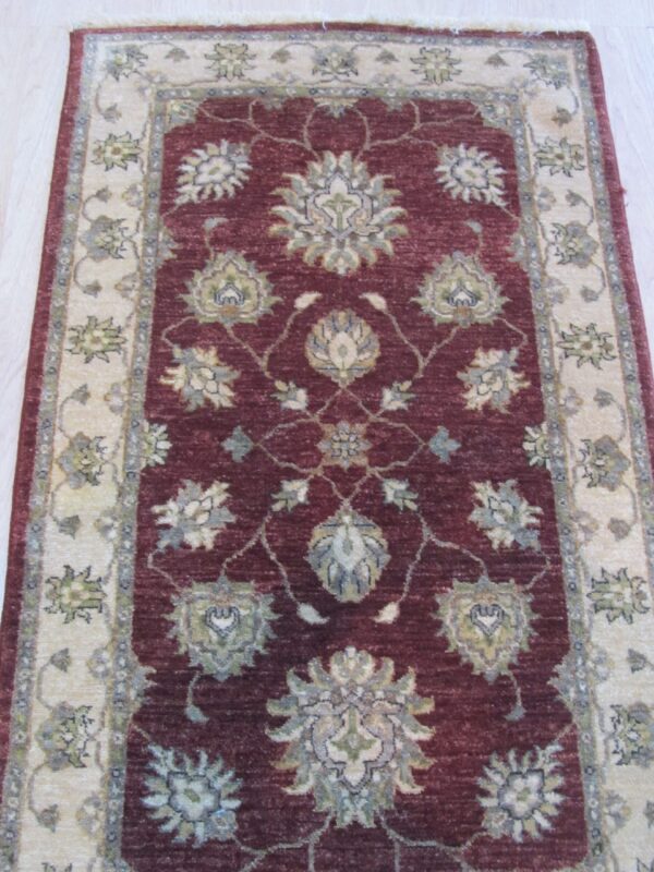 Deep burgundy runner rug featuring intricate cream, sage, and blue floral patterns on pale wood flooring.