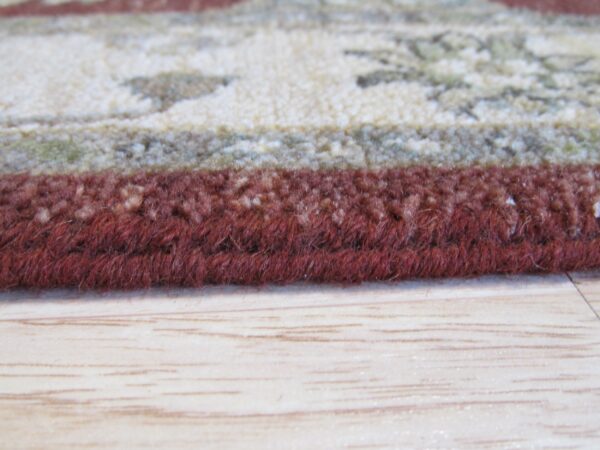 Thick, dark red rug edge next to a patterned cream area, resting on light wood flooring.