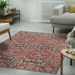 Distressed red and gray botanical rug beneath a light sectional sofa and mid-century style wooden armchair.