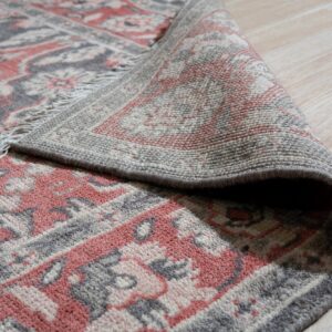 Close-up of a terracotta, gray, and cream patterned rug curled back, revealing the backing on a light wood floor.