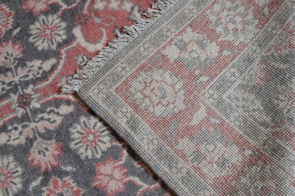 Close-up of a gray and coral rug, showing the dense patterned pile and the woven backside with fringe.