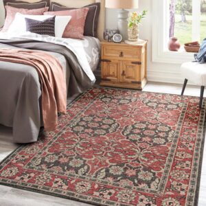 Red, gray, and beige traditional patterned area rug sits on light wood flooring in a sunny bedroom.