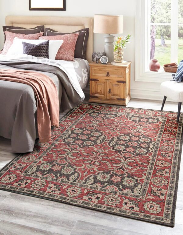 Red, gray, and beige traditional patterned area rug sits on light wood flooring in a sunny bedroom.