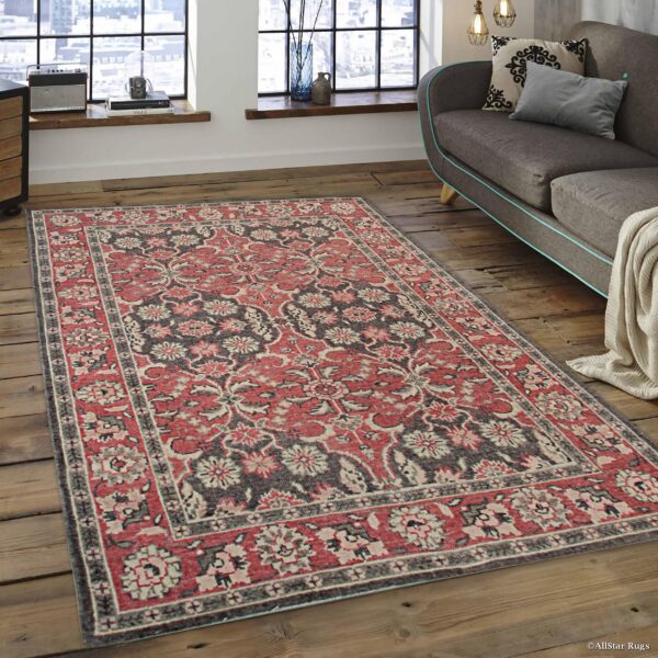 Distressed red and charcoal floral rug on rustic wood flooring in a bright loft setting with a gray sofa.