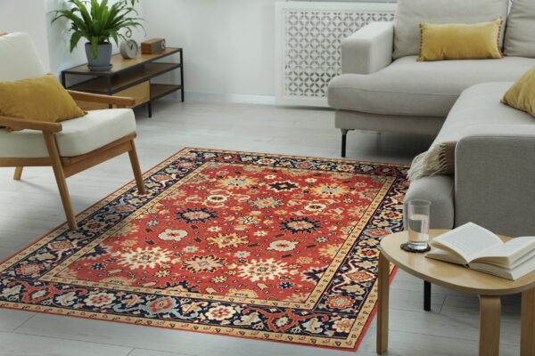 A traditional red rug featuring intricate navy and cream patterns sits on light gray wood floors.