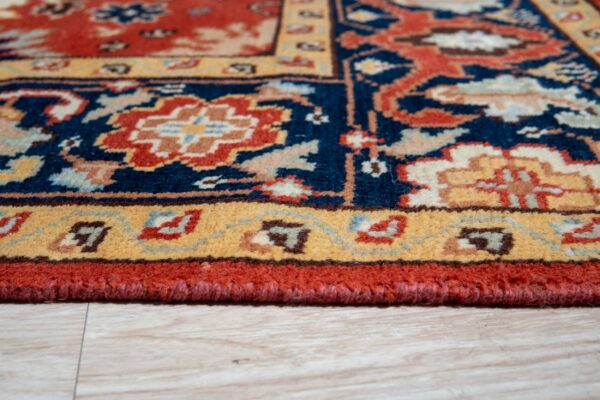 Low-pile rug detail showing ornamental navy, terracotta, and gold motifs over light wood flooring.