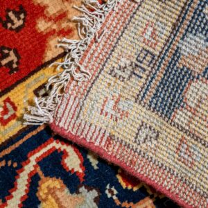 A high pile rug section with red and blue patterns is folded over, revealing its woven backing and fringe.