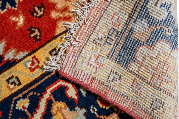 A high pile rug section with red and blue patterns is folded over, revealing its woven backing and fringe.