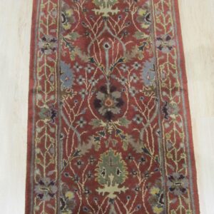 Traditional runner rug in rust and blue-green floral patterns, placed on light wooden planks.