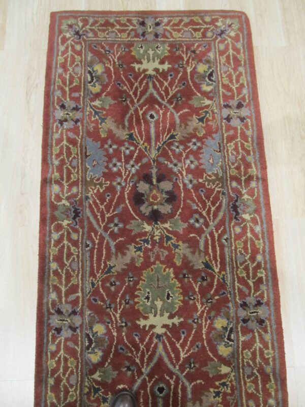 Traditional runner rug in rust and blue-green floral patterns, placed on light wooden planks.